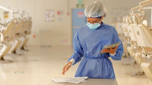 A healthcare professional in blue protective gear reviews documents in a medical clinic.