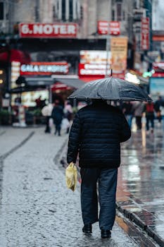 Man walking with umbrella on rainy cobblestone street in Istanbul.