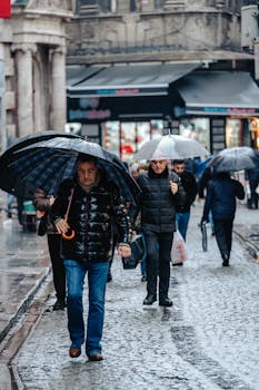 Pedestrians with umbrellas walk on a wet cobblestone street in Istanbul during the day.