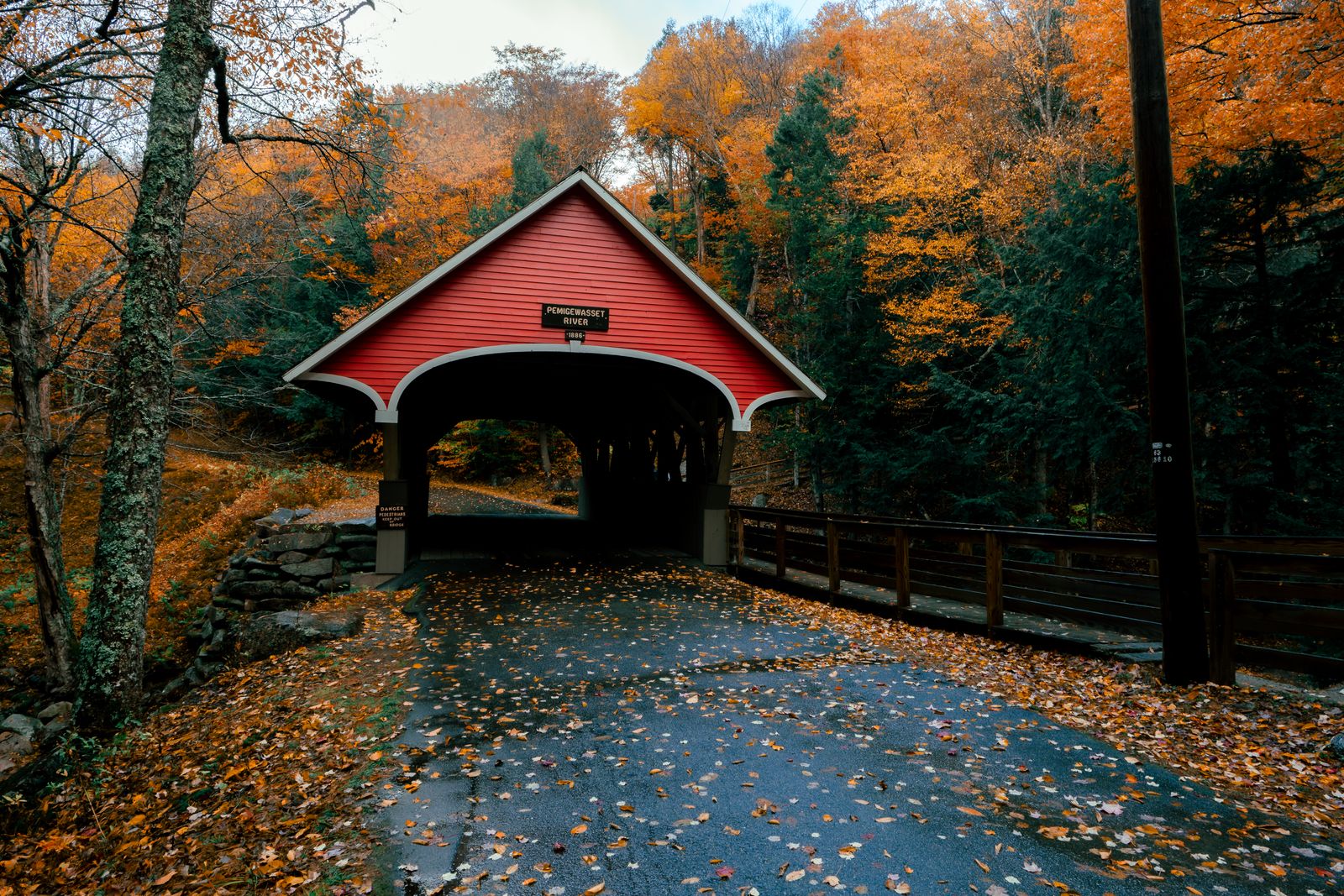 Red covered bridge framed by orange and gold autumn leaves in New England