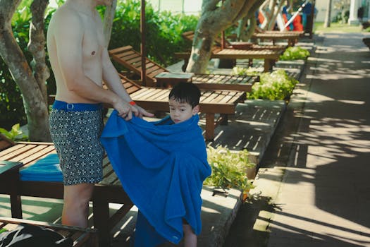 Father wraps son in towel at beach resort. Summer family fun.