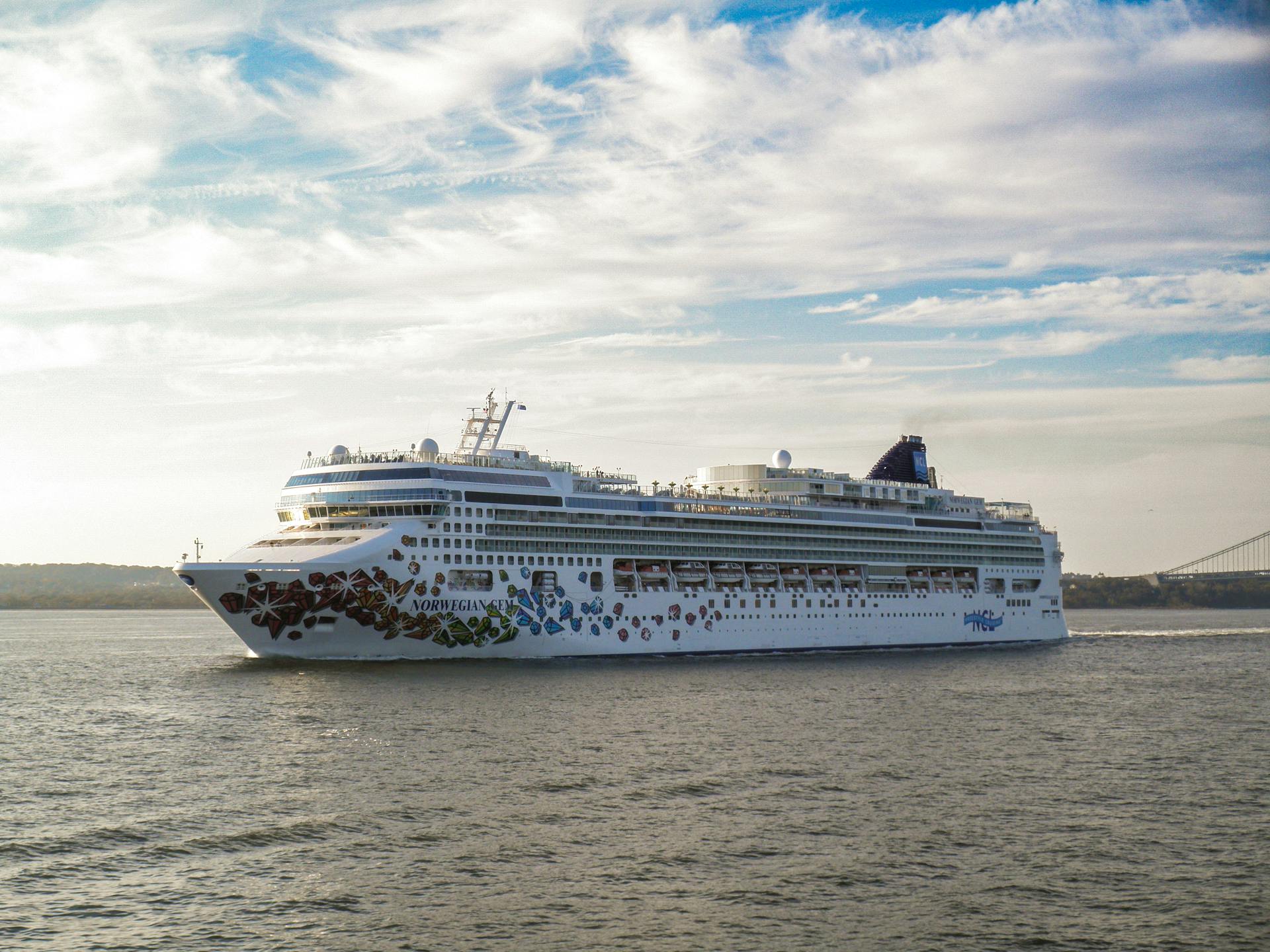 A large cruise ship gracefully sails on a calm sea under a bright sky.