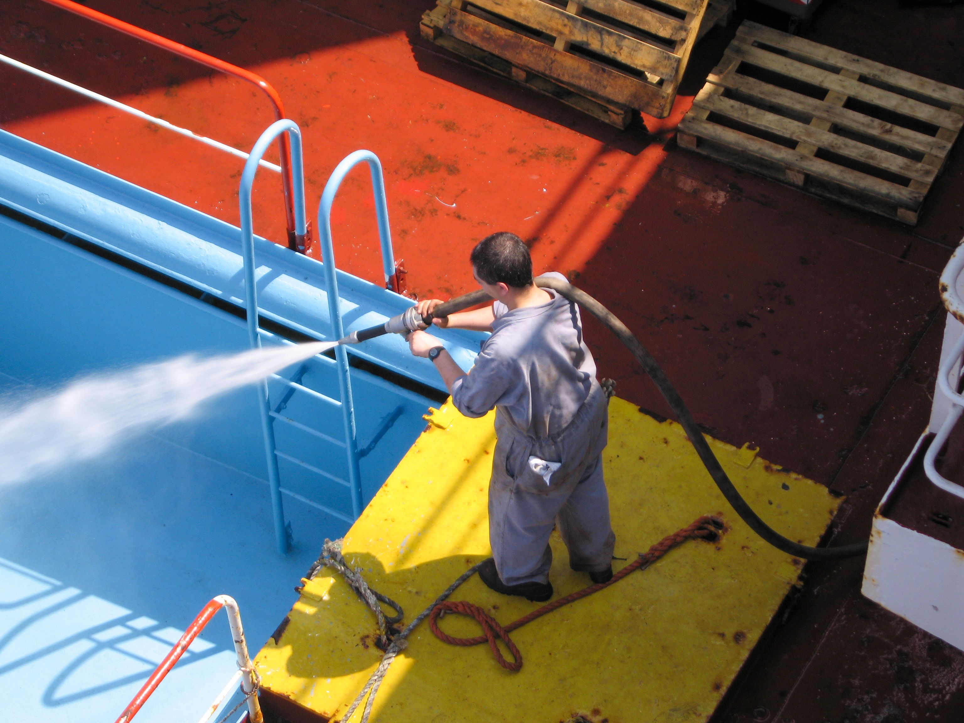 Worker performing industrial cleaning on equipment and flooring using high-pressure water in a commercial facility.
