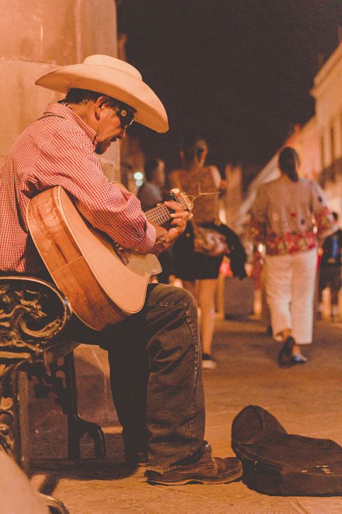 Free Elderly street musician plays acoustic guitar at night in a vibrant city setting, wearing a cowboy hat. Stock Photo