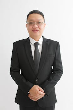 Formal portrait of a man in a black suit and tie against a plain white background.