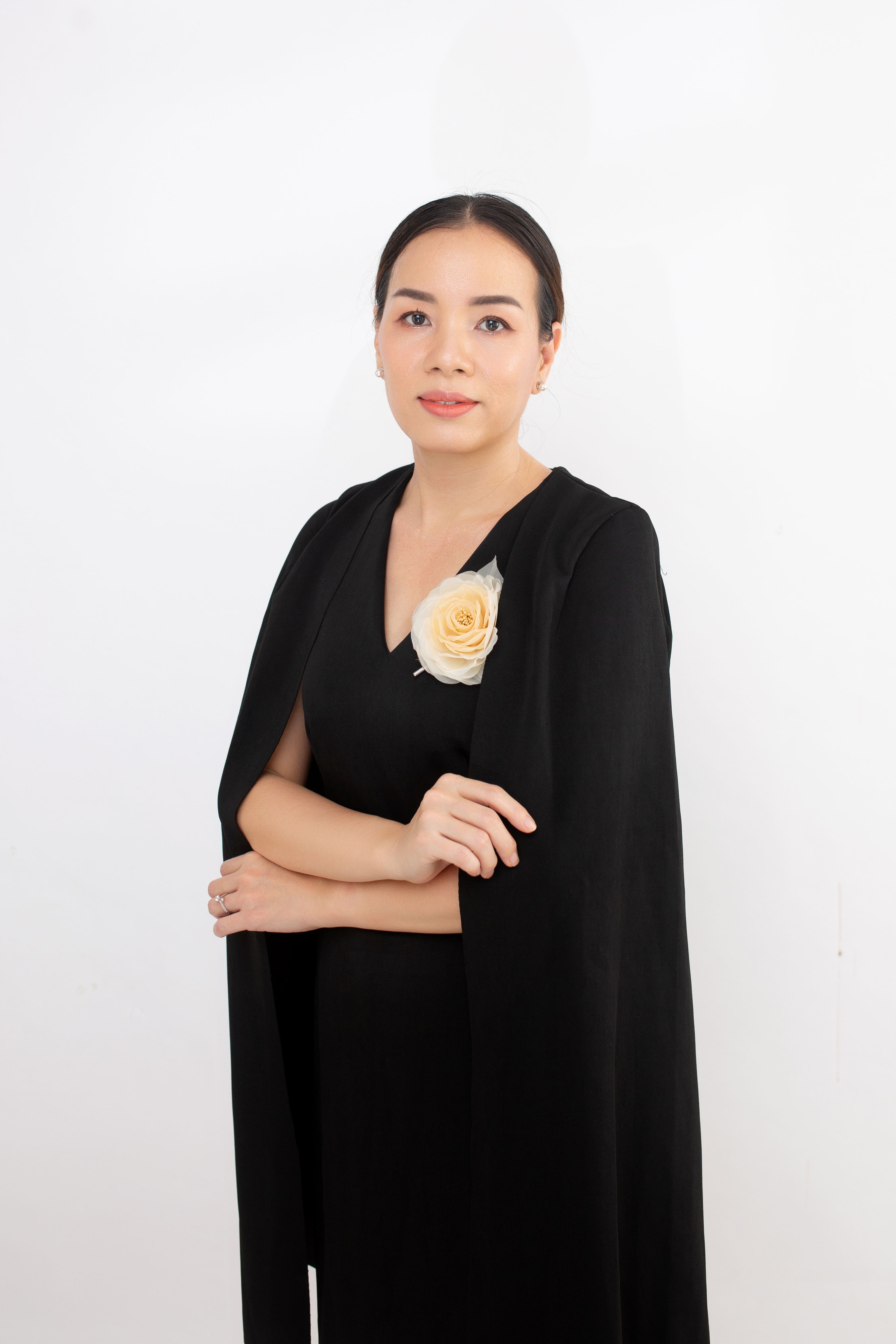 Confident woman in elegant black outfit with a peach rose brooch, posing gracefully.