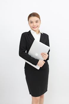 Confident young woman in business suit holding a laptop with a smile.
