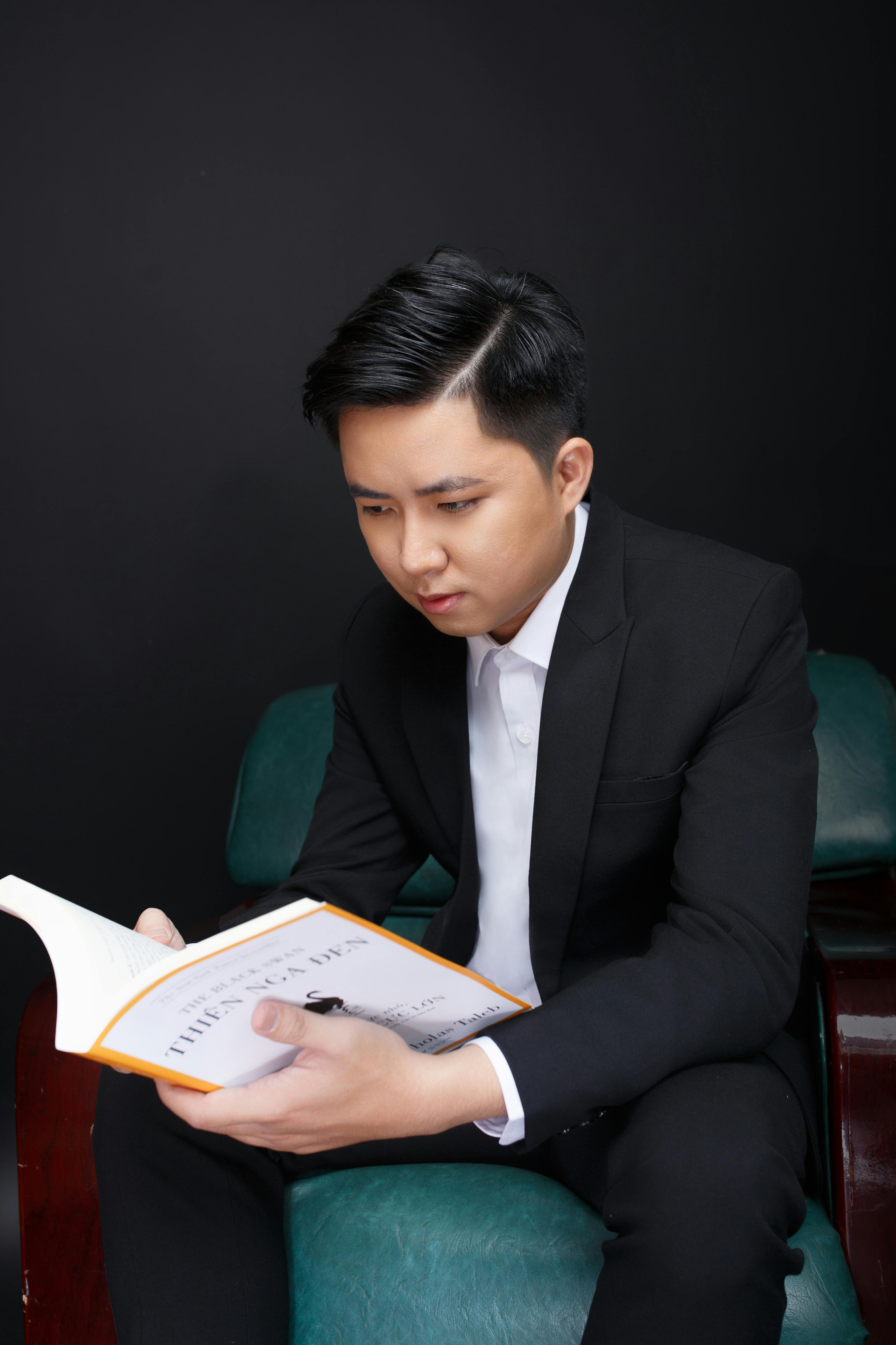 A well-dressed young man in a suit intensely reads a book indoors.
