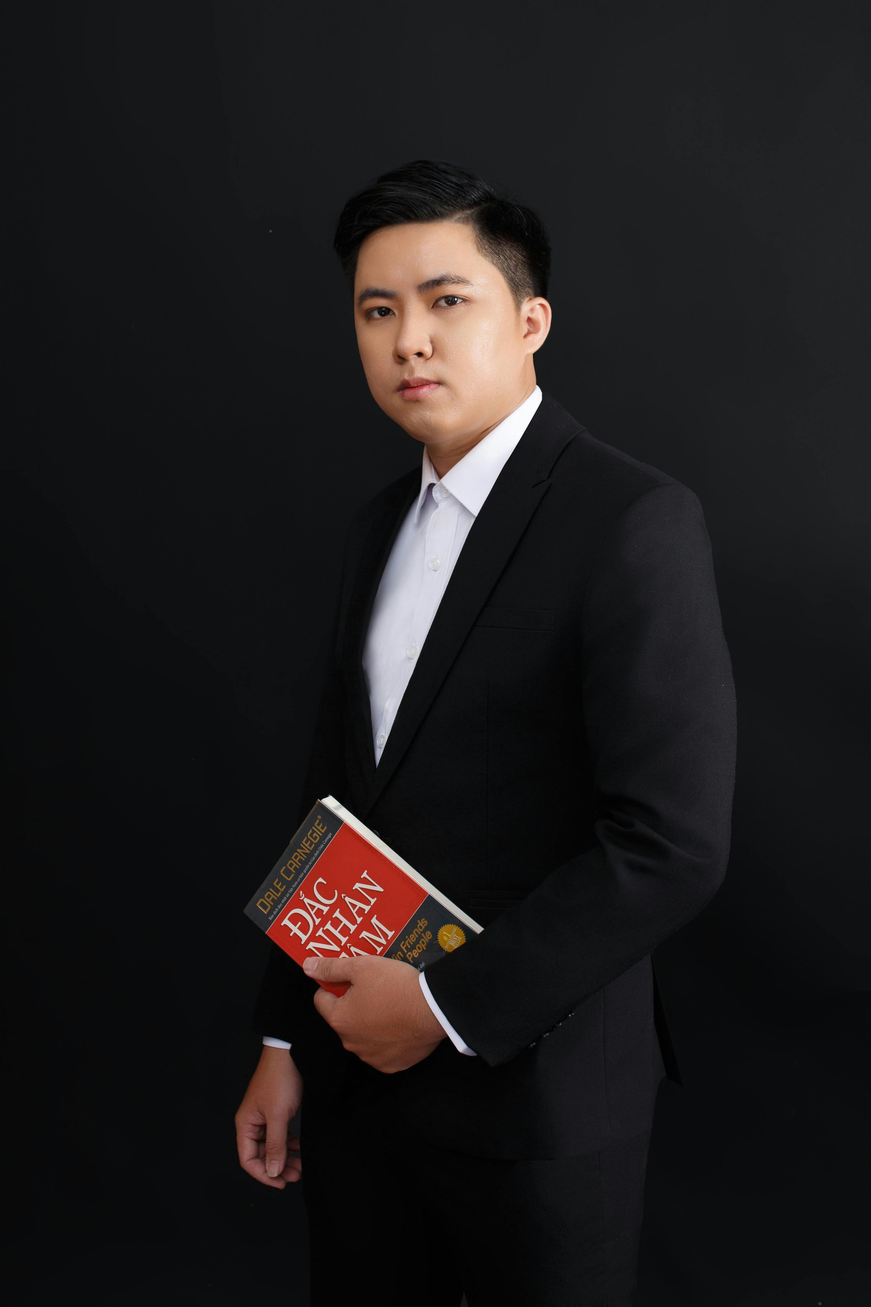 Formal portrait of a young adult male in a black suit holding a book.