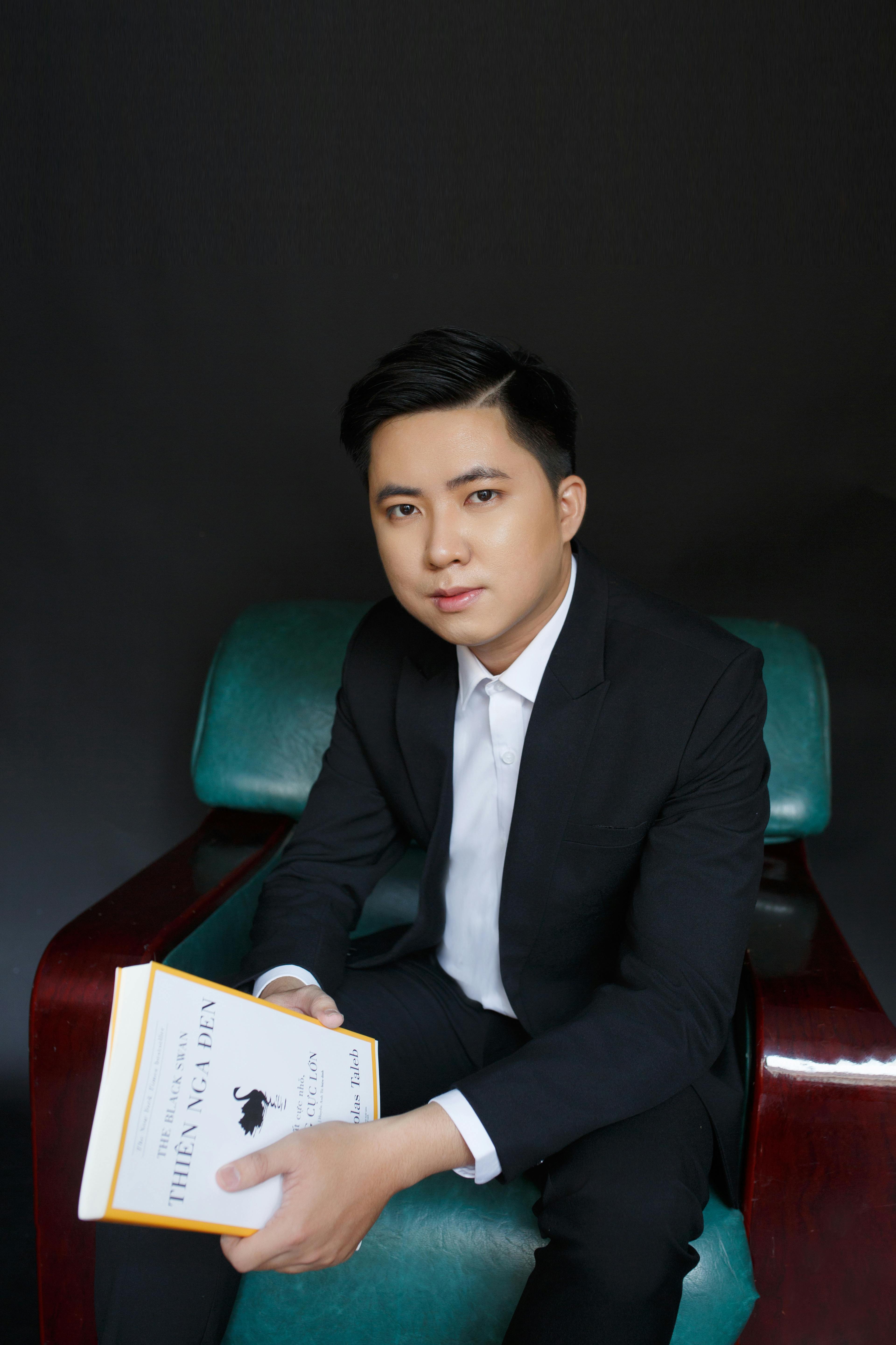 Professional portrait of a young male businessman holding a book in a chair.