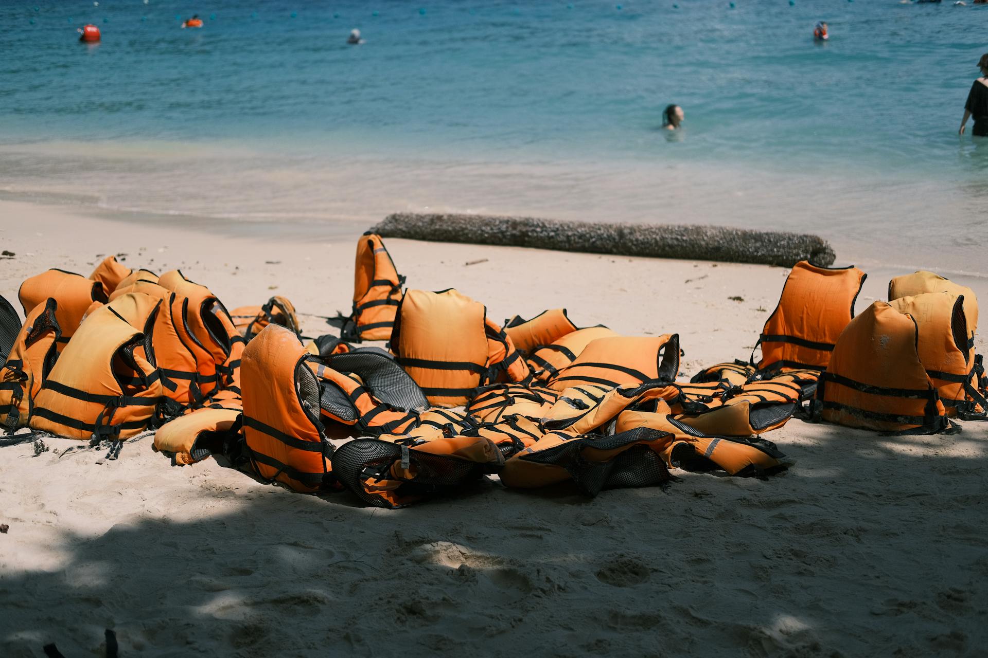 Bright orange life jackets scattered on a sandy beach near the ocean, embodying summer safety and adventure.