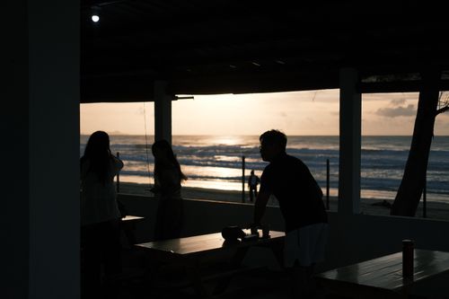 Free A serene sunset view from a beachside cafe with silhouettes of people enjoying the scene. Stock Photo