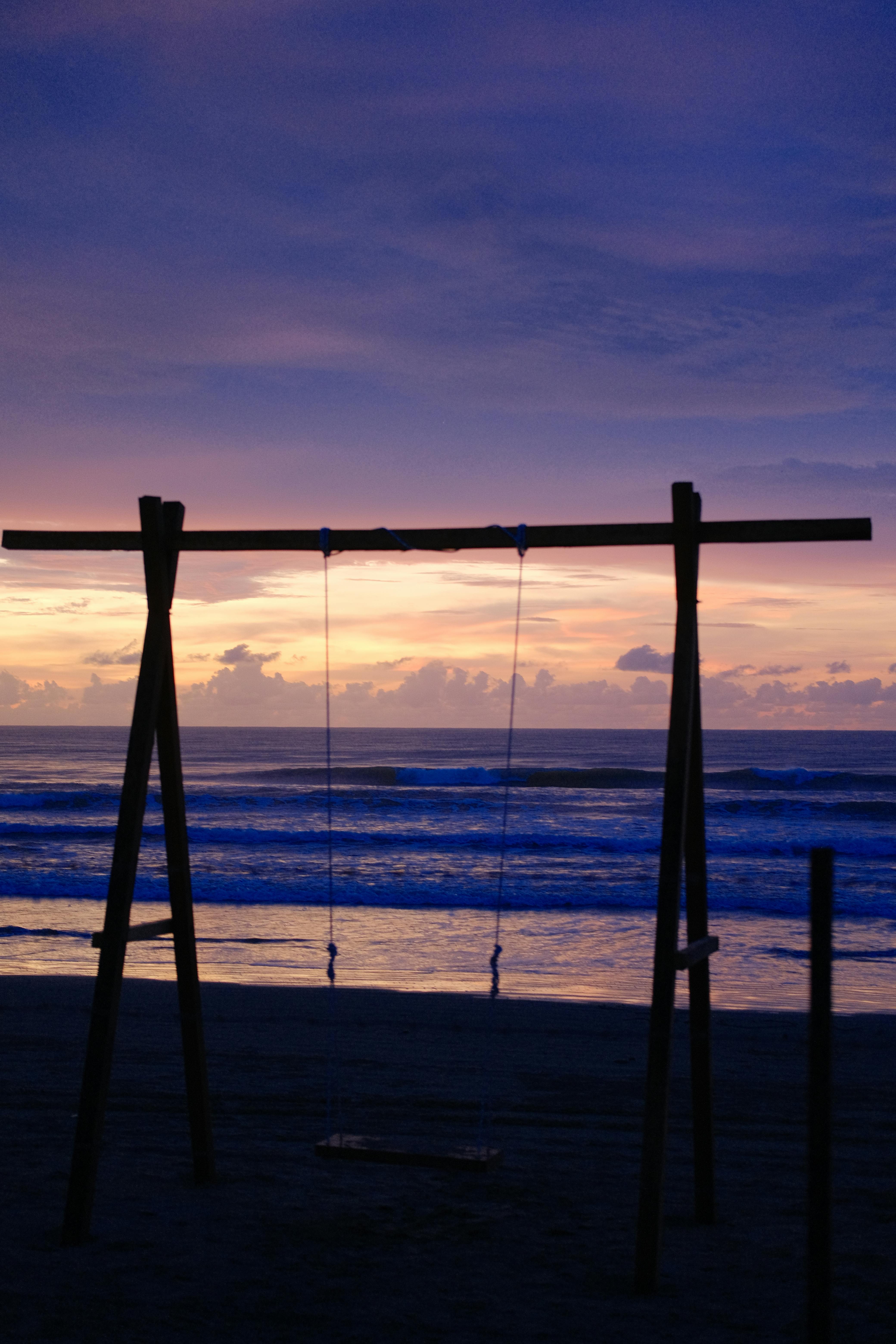 Silhouette of a beach swing set against a colorful sunset sky, capturing tranquil seaside evening mood.