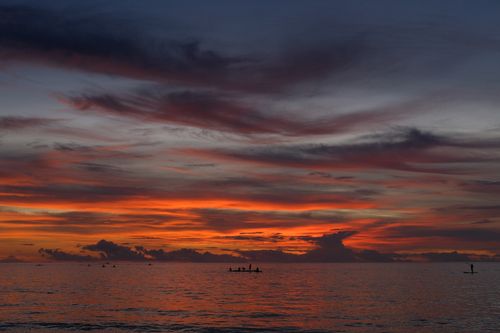 Free Beautiful sunset over ocean with silhouetted people paddling, creating a peaceful scene. Stock Photo