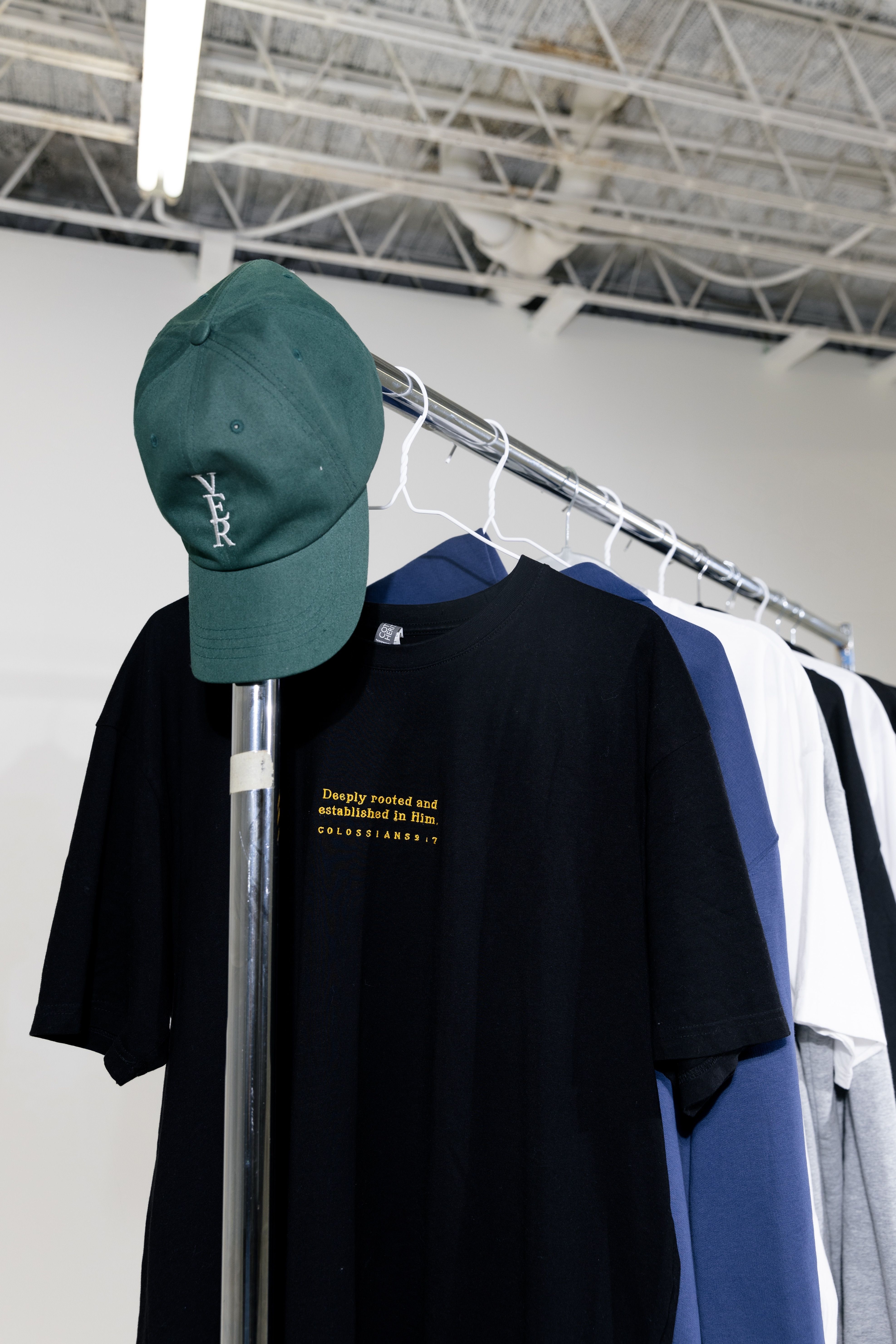 A variety of colorful T-shirts and a cap on a display rack in a modern store.