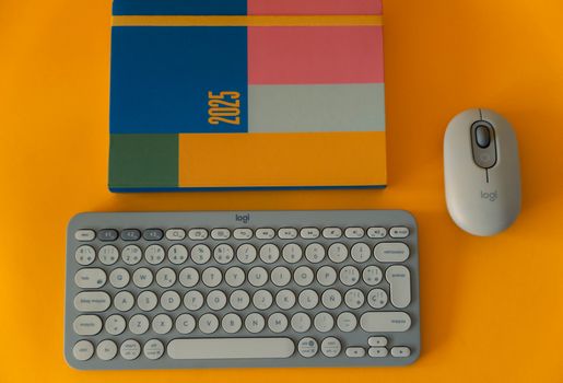 Flat lay of a 2025 planner, keyboard, and mouse on a vibrant yellow background.