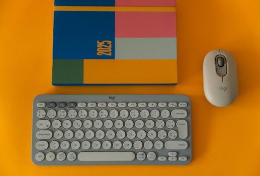 Flat lay of a colorful 2025 planner with keyboard and mouse on a bright orange background.