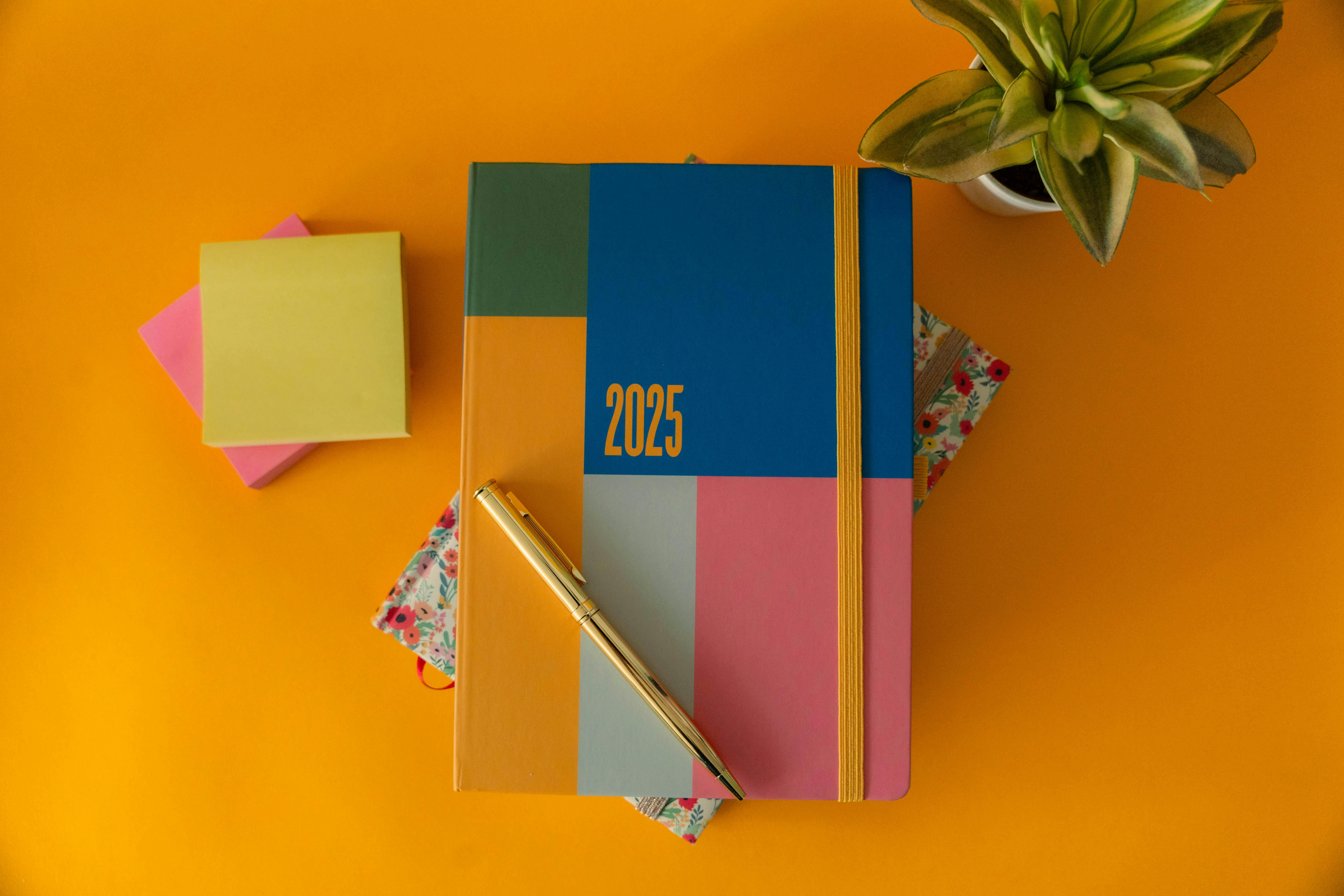 A colorful 2025 planner with a pen and sticky notes on a vibrant yellow background.