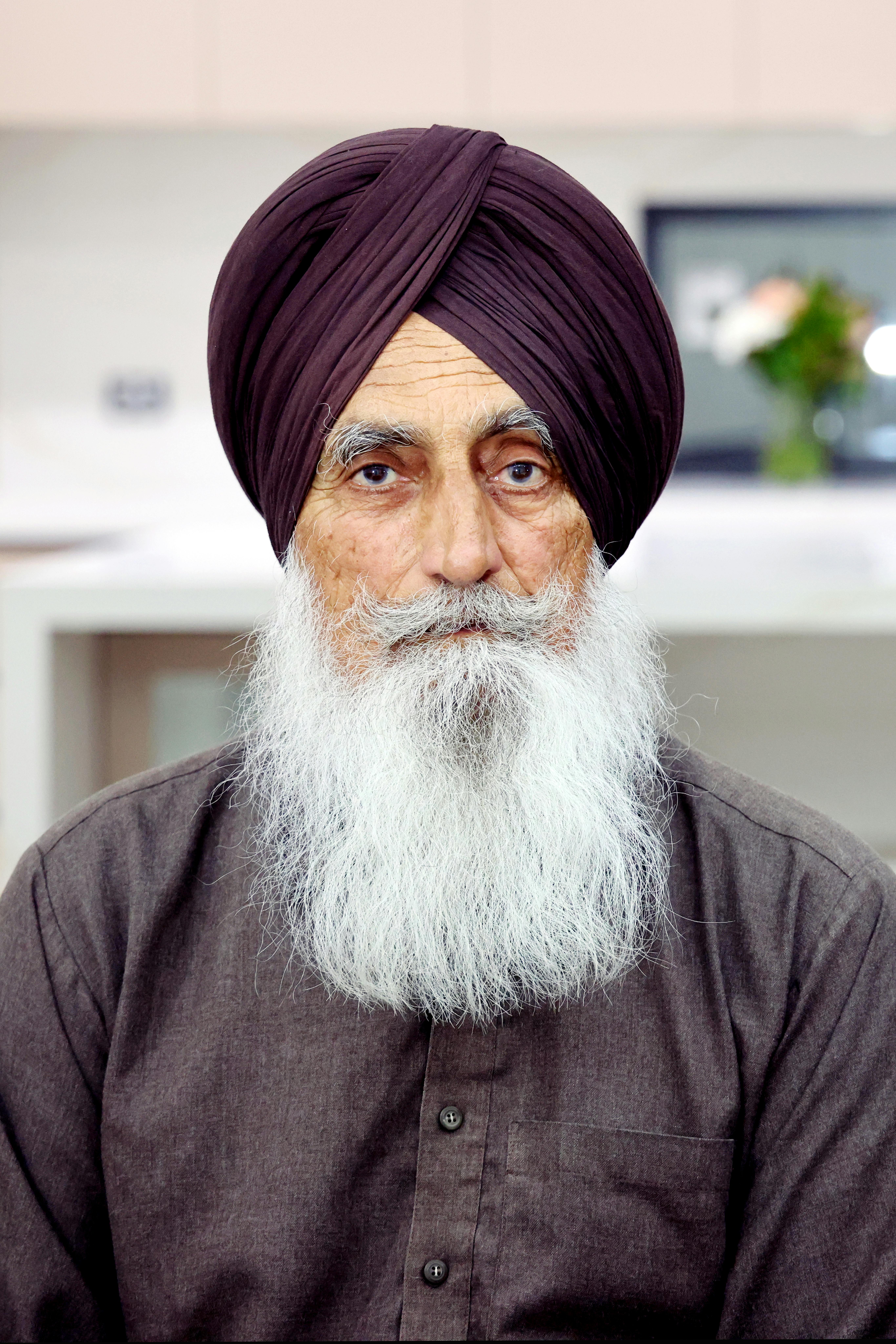 Portrait of an elderly Sikh man wearing a turban, seated indoors, exuding wisdom and grace.