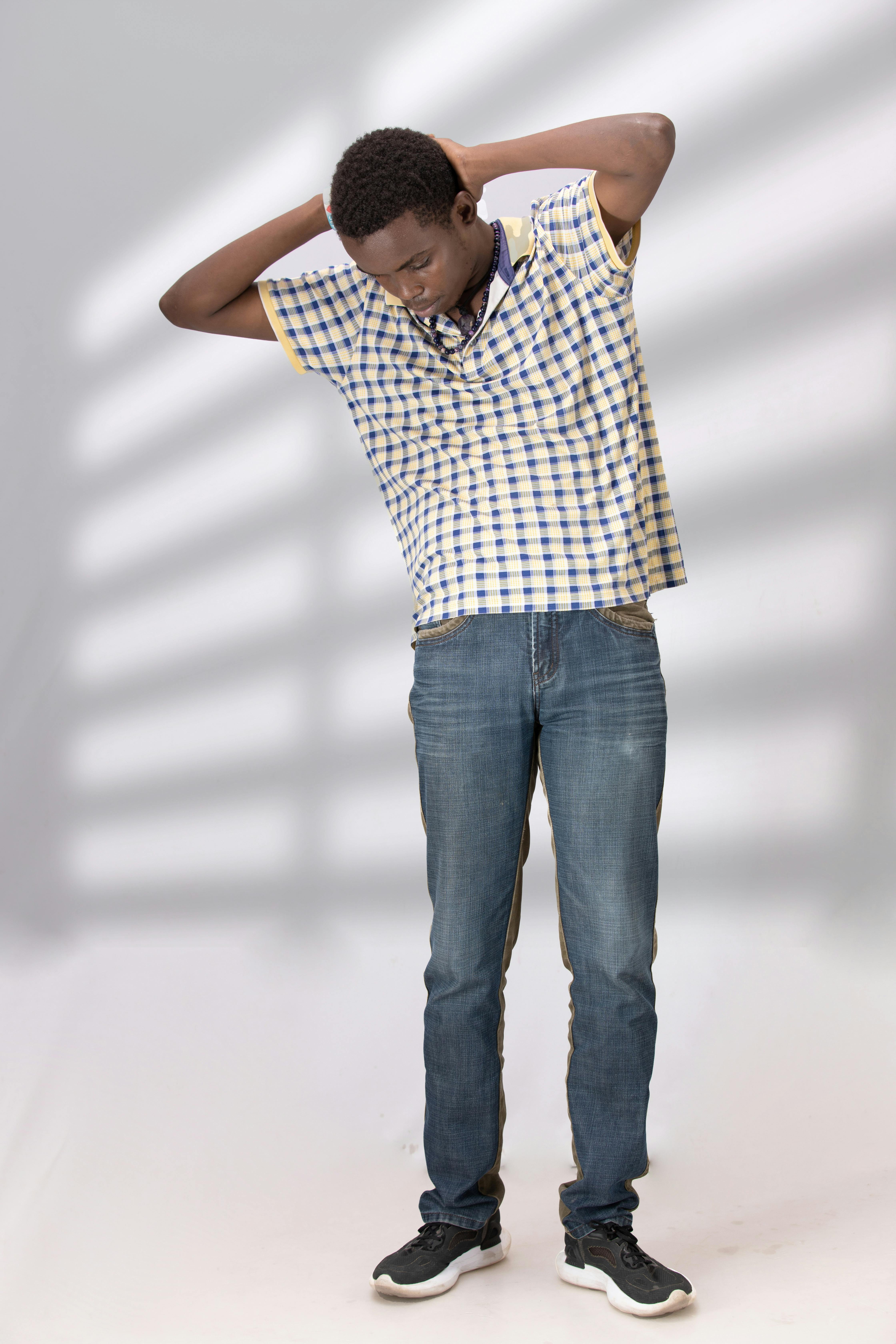 grátis Jovem elegante com camisa xadrez e calça jeans posando em ambiente fechado com luz natural. Foto profissional