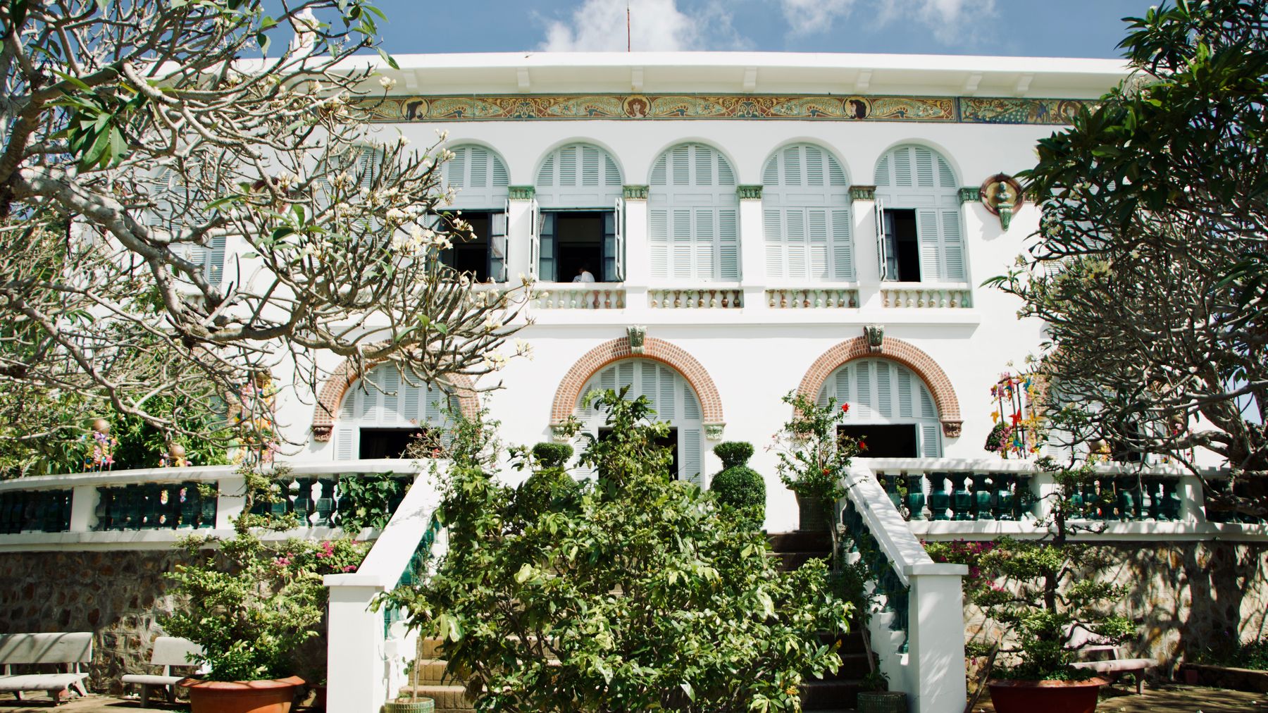 A classic colonial-style house surrounded by tropical plants and trees.