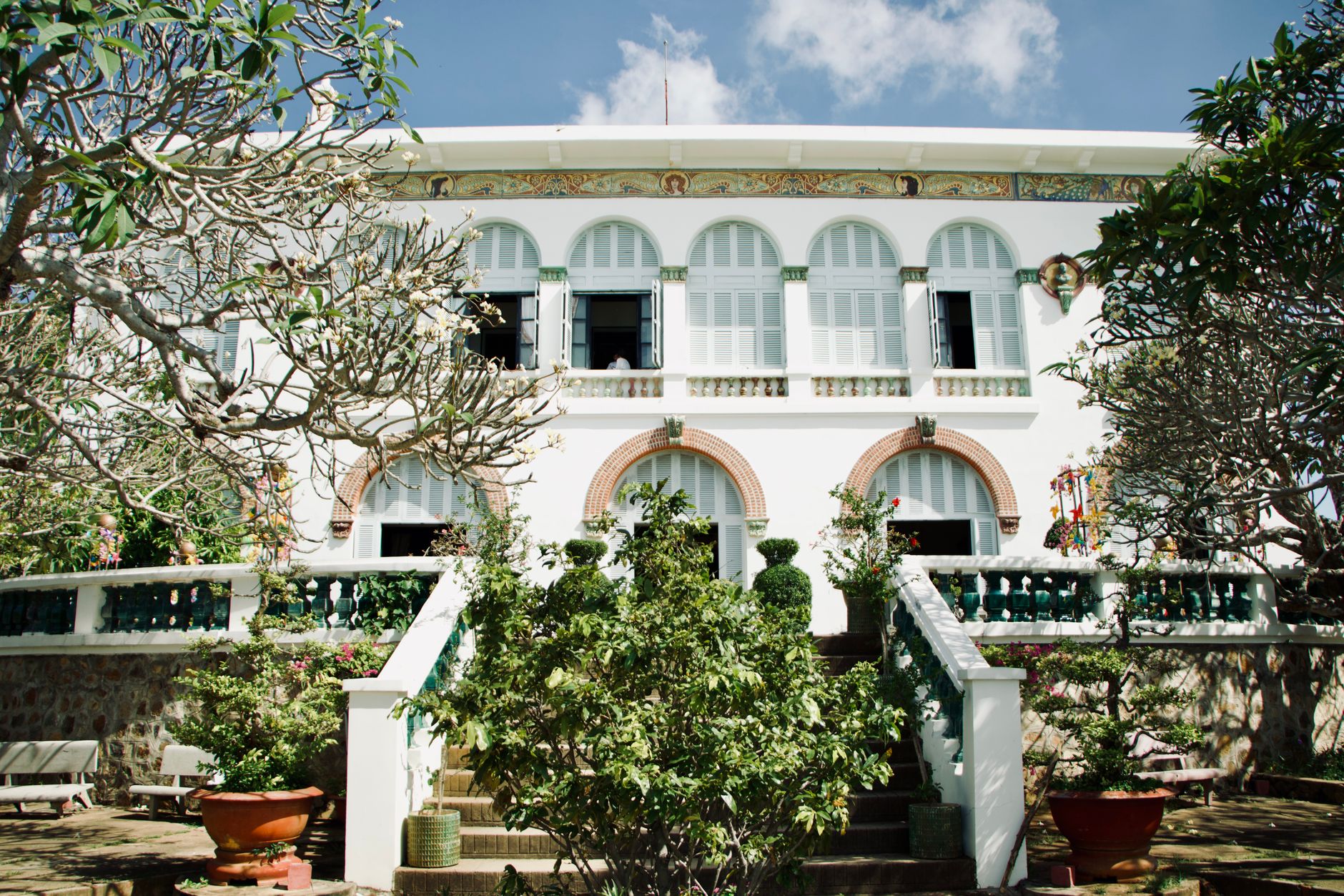 A classic colonial-style house surrounded by tropical plants and trees.