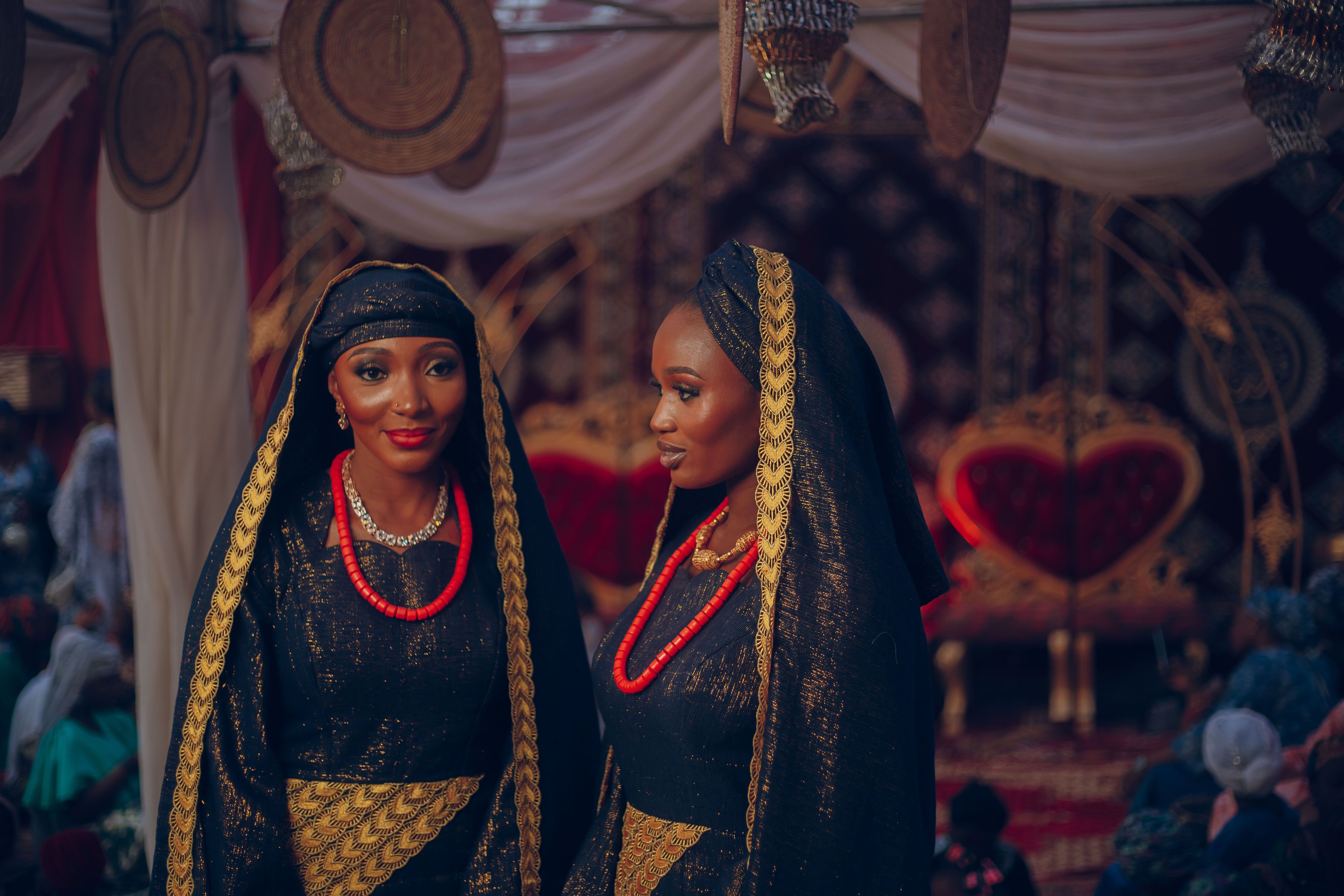 Two women in traditional Nigerian attire at a vibrant wedding ceremony.