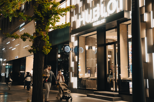 A lively street in Osaka, Japan, with people walking by a Hublot store at night.