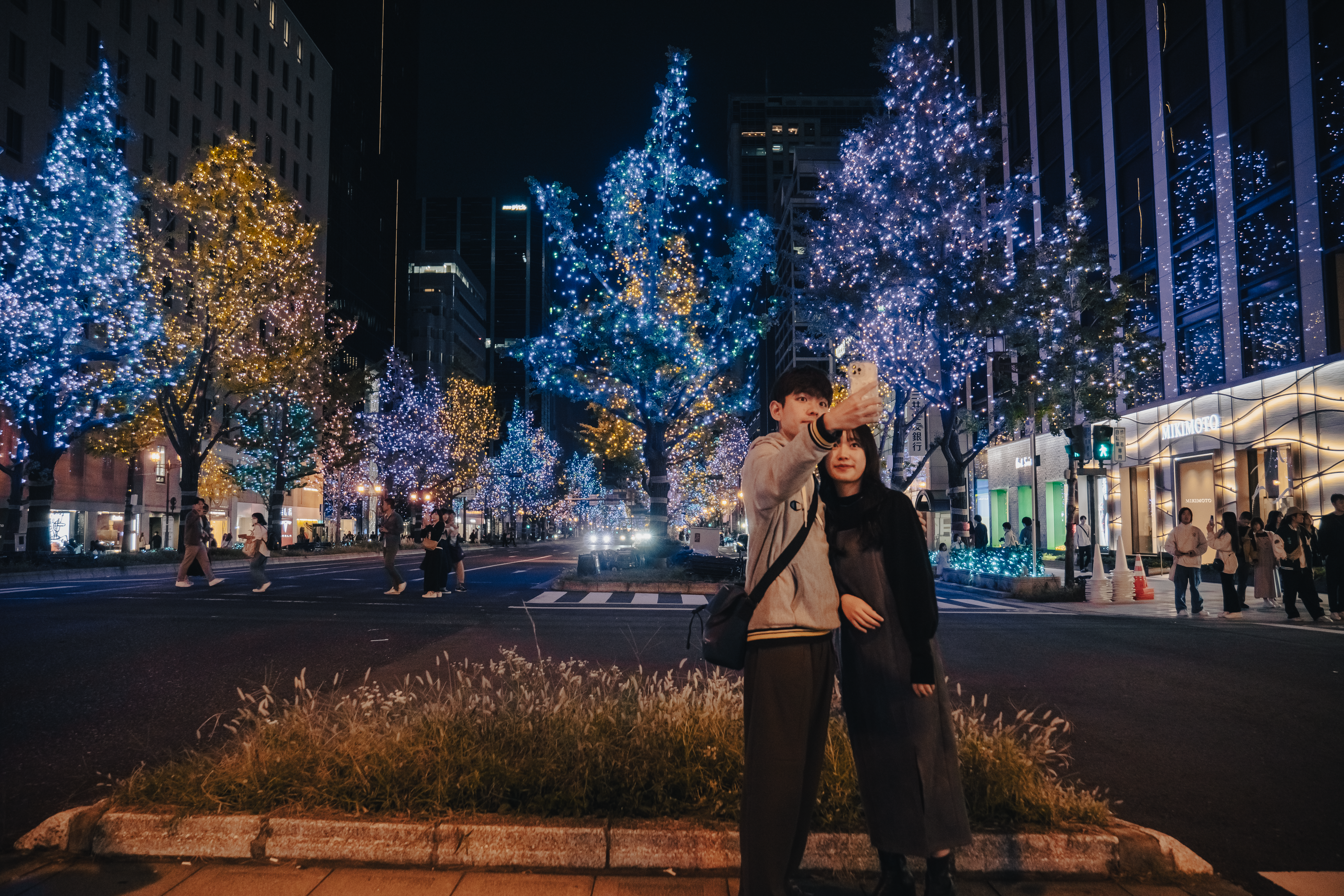 A couple takes a selfie on a vibrant, illuminated street in Osaka, Japan, surrounded by festive lights.