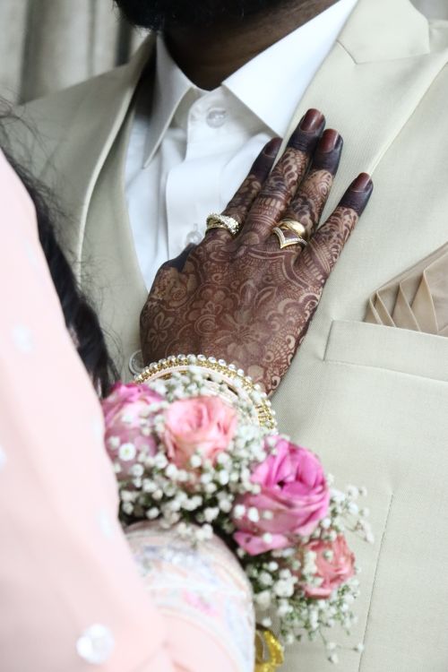Free Beautiful bridal henna hand resting on groom's chest with floral bouquet. Stock Photo