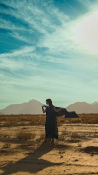 A woman stands dramatically in a vast desert landscape, capturing a serene and cinematic moment.