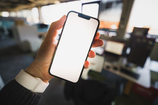 A blank smartphone screen held in an office environment, perfect for mockup presentations.