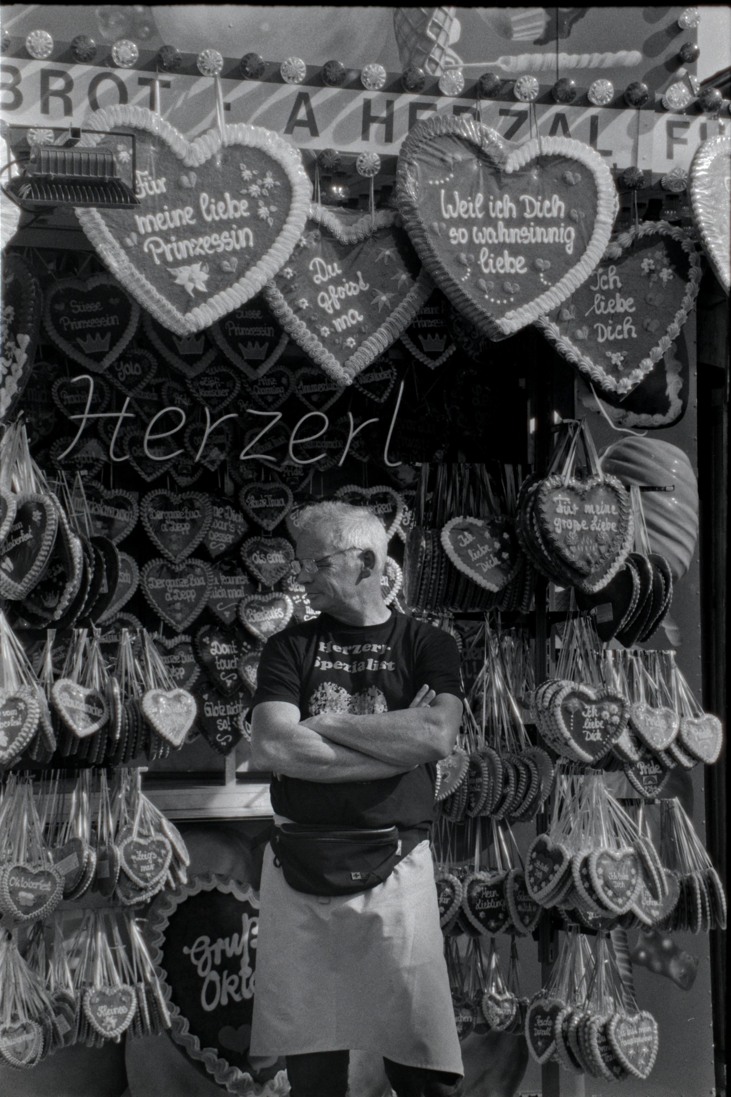 Man standing by a gingerbread heart stall at Oktoberfest in Germany.