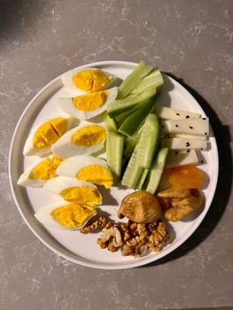 Colorful platter with boiled eggs, cucumbers, cheese, nuts, and dried fruits.
