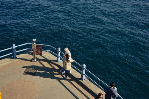 Free Top view of people on a sunny pier overlooking vibrant blue ocean waves. Stock Photo