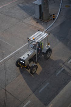 A worker operates an industrial vehicle on the airport tarmac during sunset.