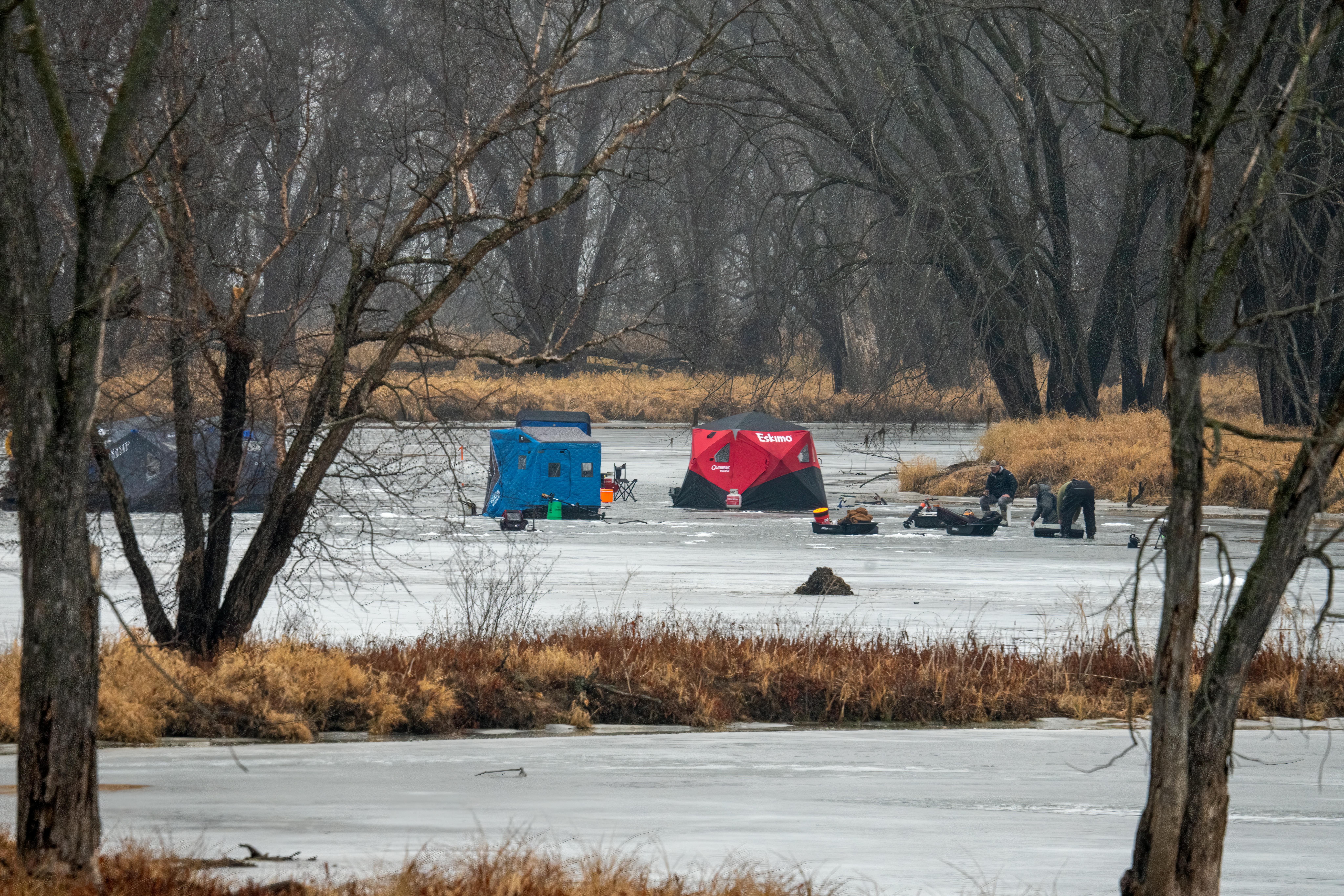 A serene winter scene with ice fishing tents on a frozen lake surrounded by trees.