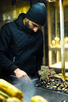 Man selling roasted chestnuts from a street stall at night.