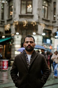 A man stands confidently in a city street decorated with festive lights, creating a warm urban atmosphere.