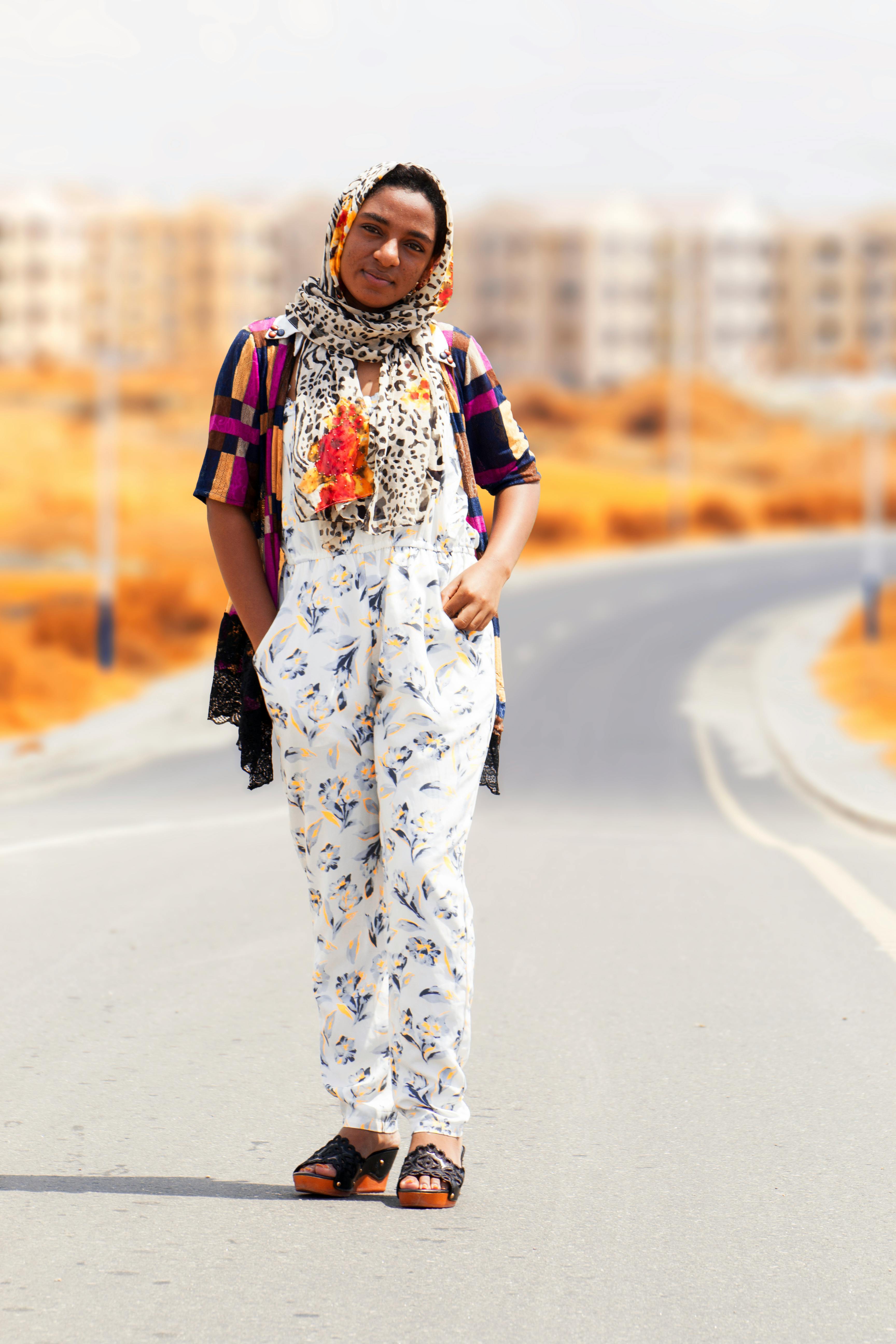 一位时尚女士在阳光明媚的城市道路上自信地摆出姿势，展示着充满活力的服装