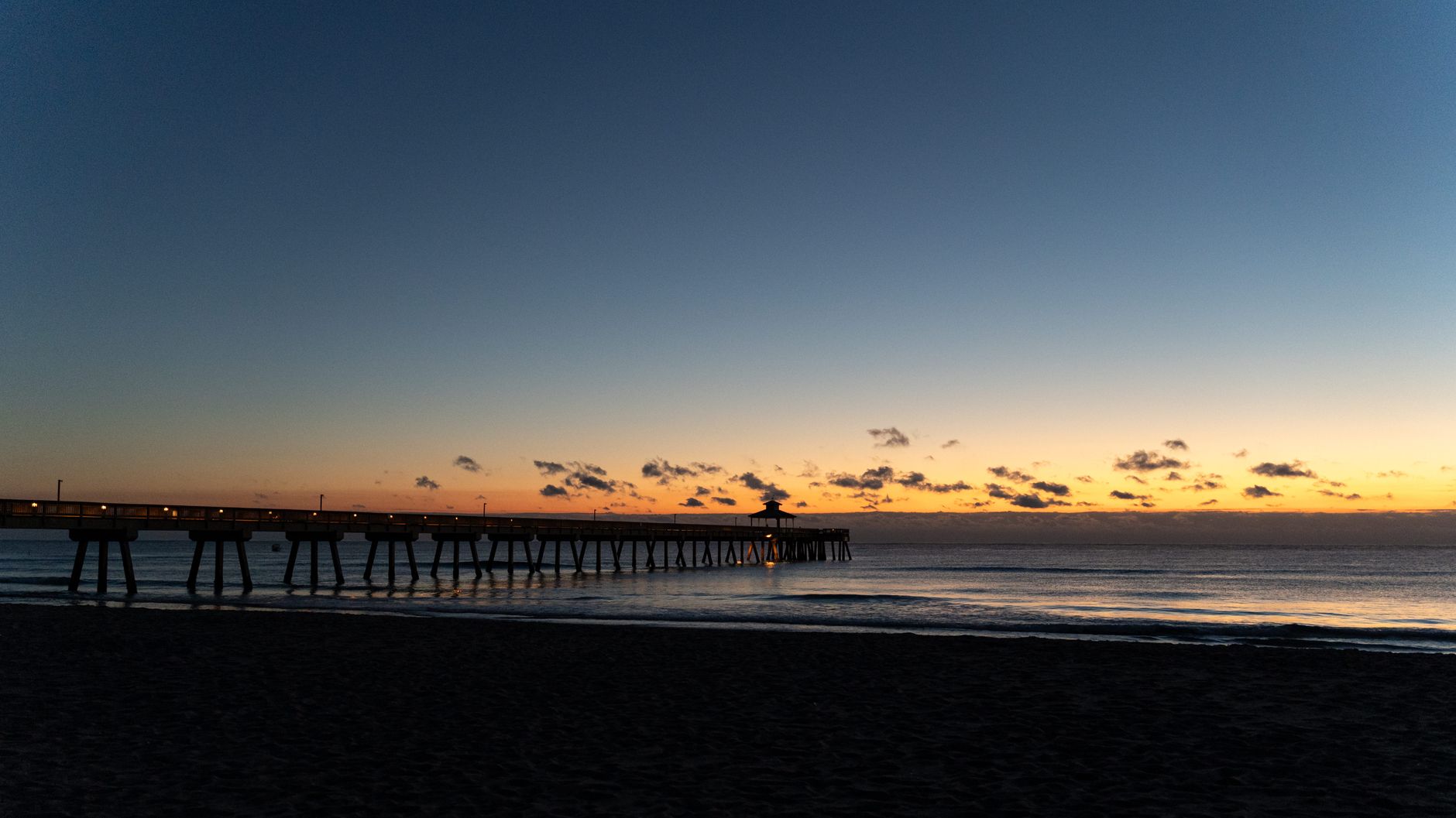 Peaceful sunset view of a silhouette pier stretching into the calm ocean waters.