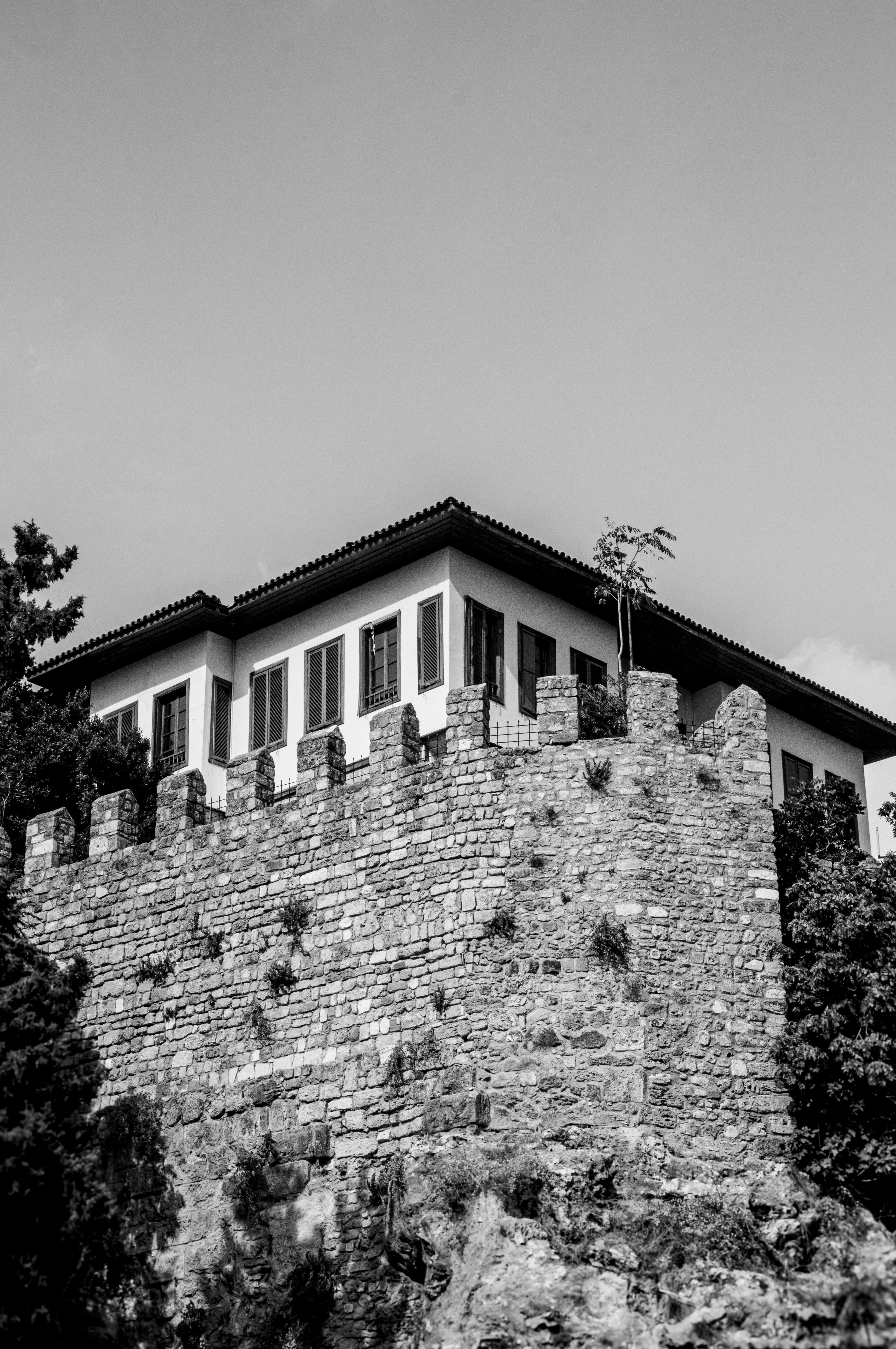 Black and white image of a historic stone fortress with a modern building on top, showcasing architectural contrast.