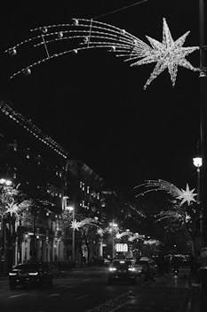 Black and white photo of a city street with festive Christmas star decorations at night.