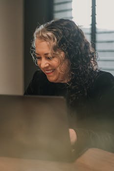 Smiling woman using a laptop while working indoors, showcasing a professional setting.