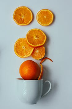 Vibrant sliced oranges artfully arranged in a white cup on a light background.