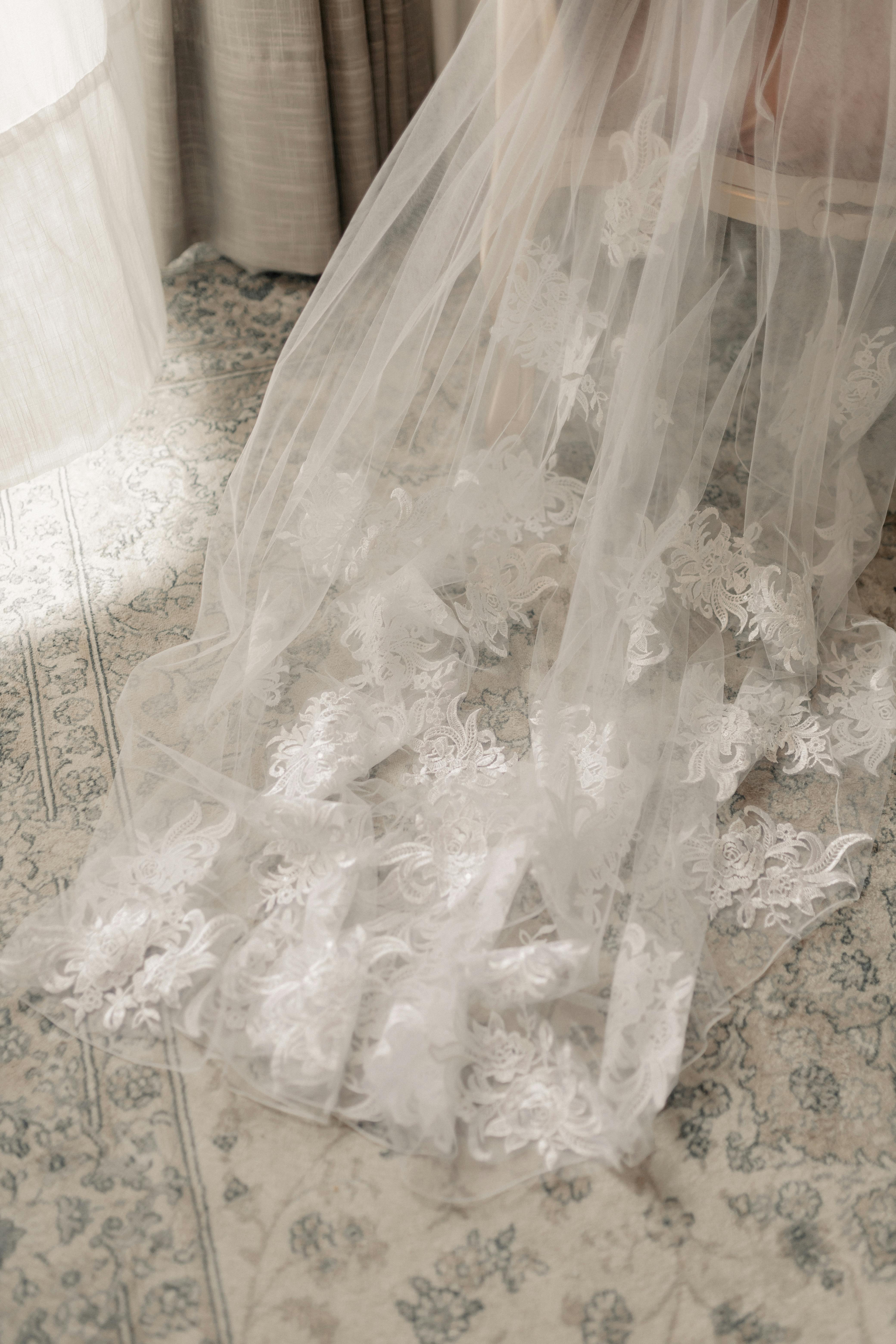 Beautiful bridal veil with lace detail gracefully spread on vintage carpet in soft light.