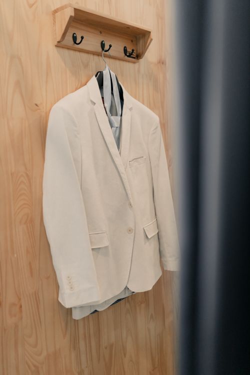 Free A stylish white suit jacket hanging on a wooden rack, perfect for formal occasions. Stock Photo
