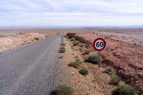 Free A long desert road in Morocco with a 60 km/h speed limit sign under a clear sky. Stock Photo