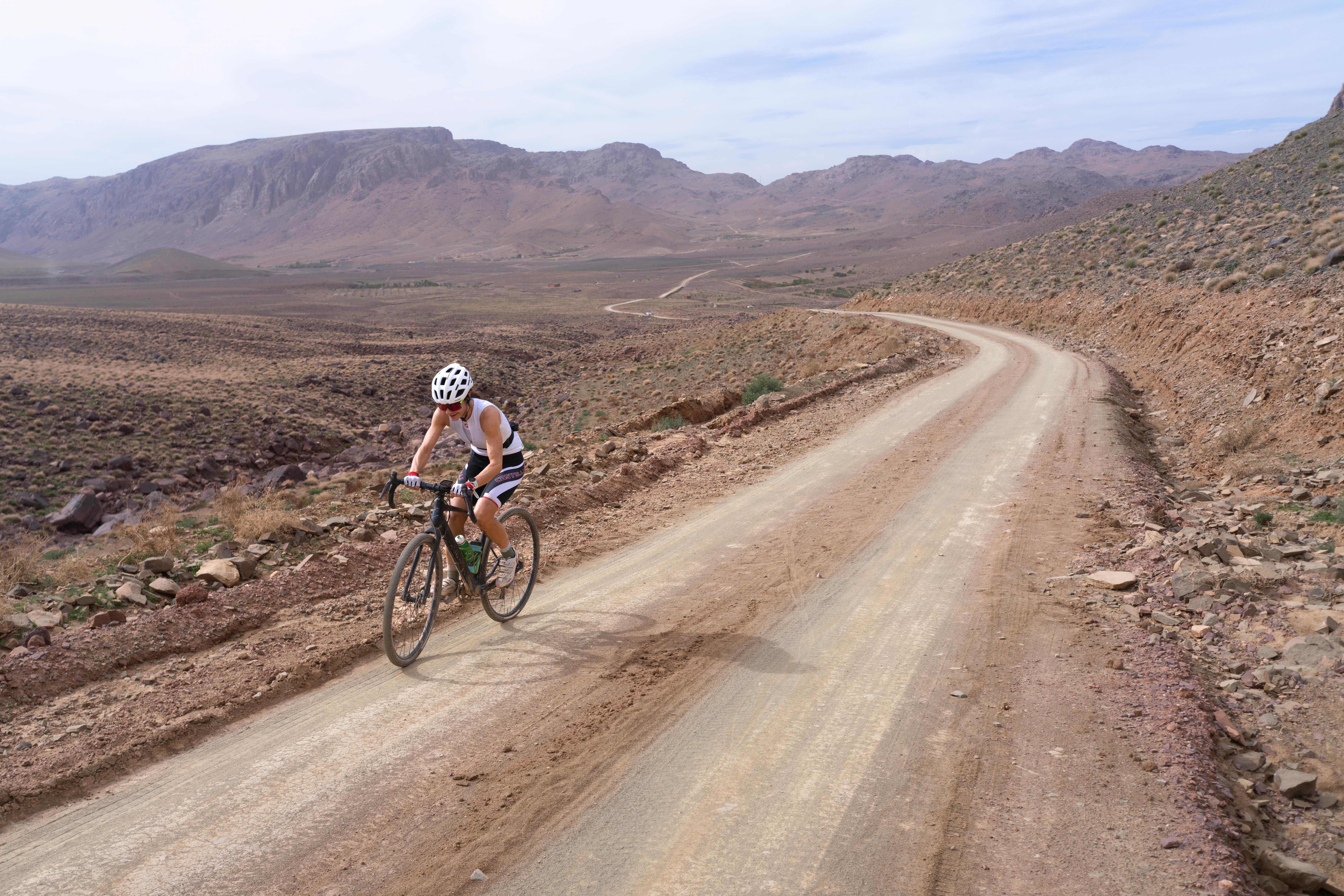 Cyclist biking on a rugged desert trail surrounded by rocky landscape under a cloudy sky.