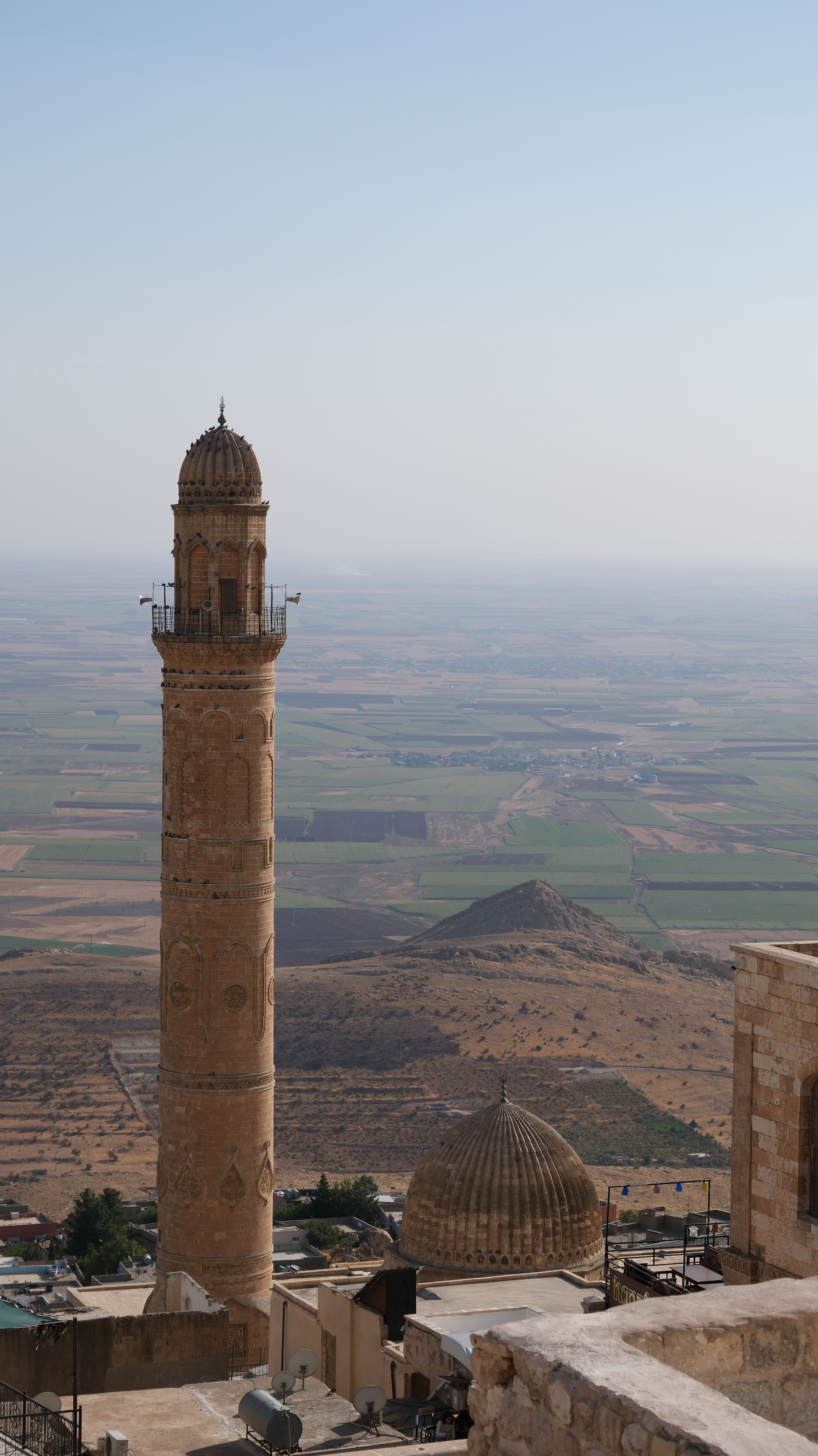 A scenic view of a historic minaret and dome overlooking the vast landscapes of Mardin.